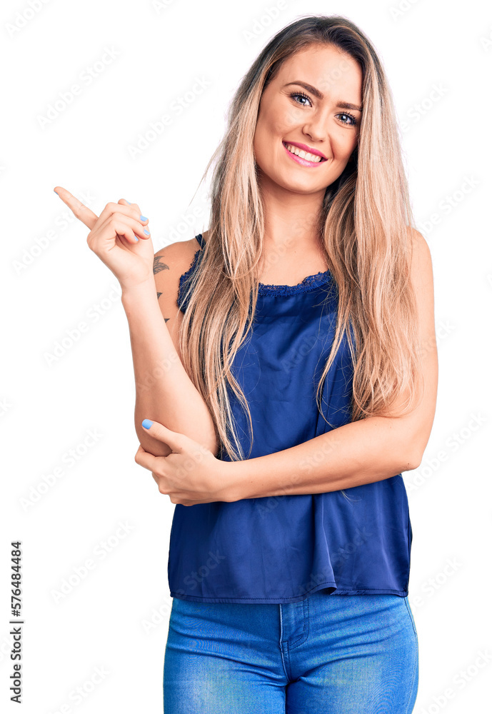 Young beautiful blonde woman wearing casual sleeveless t-shirt smiling happy pointing with hand and finger to the side Young beautiful blonde woman wearing casual sleeveless t-shirt smiling happy pointing with hand and finger to the side