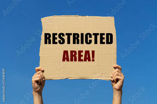 Restricted area on box paper held by 2 hands with isolated blue sky background. This message board can be used as business concept to inform everyone that this area is restrcited. photo