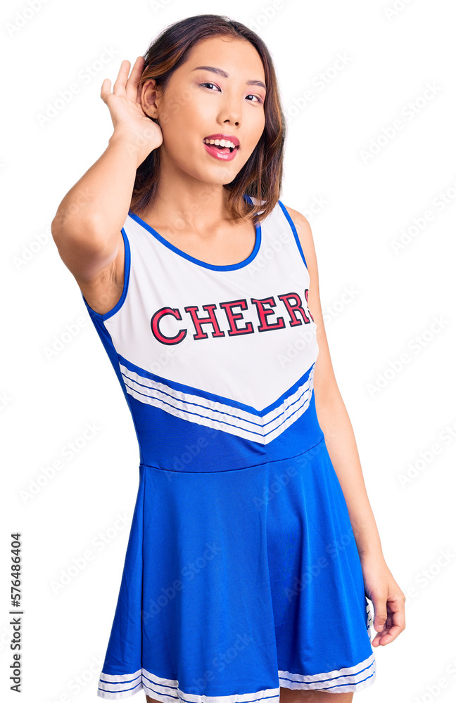 Young beautiful chinese girl wearing cheerleader uniform smiling with hand over ear listening an hearing to rumor or gossip. deafness concept. Young beautiful chinese girl wearing cheerleader uniform smiling with hand over ear listening an hearing to rumor or gossip. deafness concept.