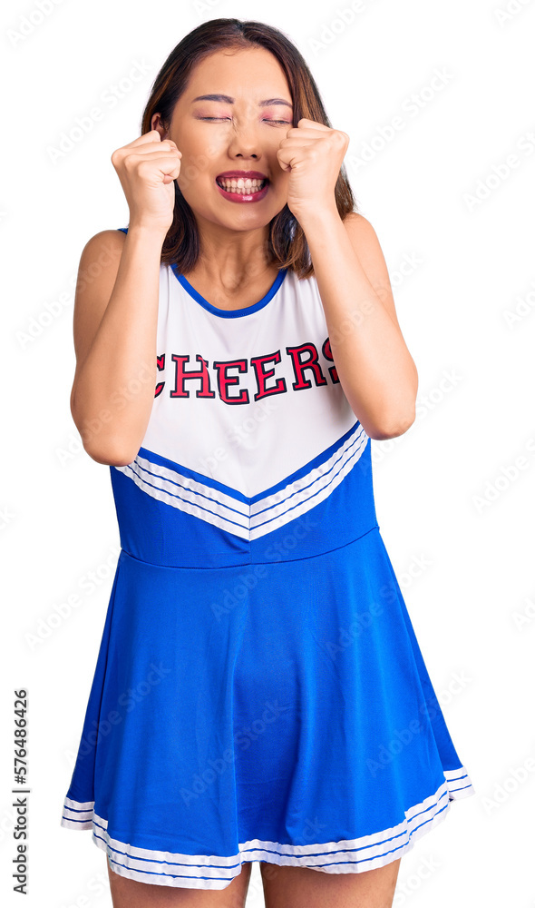 Young beautiful chinese girl wearing cheerleader uniform excited for success with arms raised and eyes closed celebrating victory smiling. winner concept.