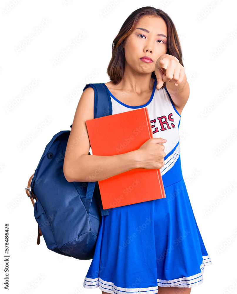 Young beautiful chinese girl wearing cheerleader uniform and student backpack holding binder pointing with finger to the camera and to you, confident gesture looking serious Young beautiful chinese girl wearing cheerleader uniform and student backpack holding binder pointing with finger to the camera and to you, confident gesture looking serious