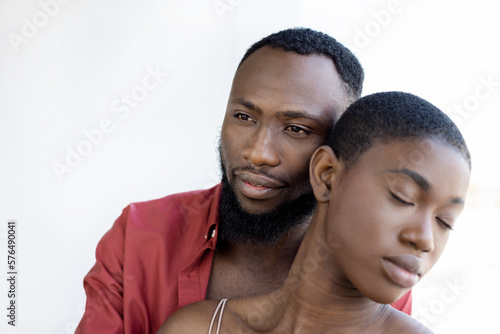 African American couple cuddling with closed eyes near window on sunny day