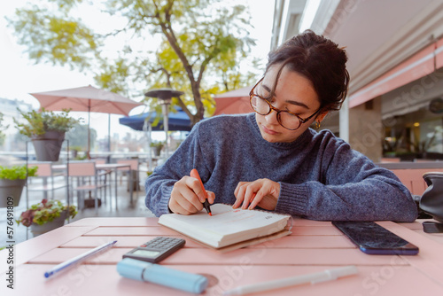 фотографія joven mujer, de 20 años, sentada en un cafe, con un libro, anotando ideas y estudiando
