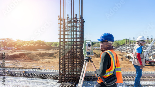 A Latino topographer measures the elevation and contours of a land area with a surveying instrument. He wears a hard hat, a reflective vest and protective glasses. He works with precision and accuracy