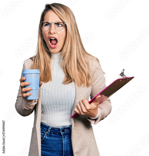 Obraz na płótnie Young blonde woman wearing business style, drinking coffee and holding clipboard angry and mad screaming frustrated and furious, shouting with anger