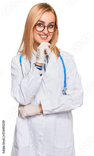 Beautiful caucasian woman wearing doctor uniform and stethoscope looking confident at the camera with smile with crossed arms and hand raised on chin. thinking positive.