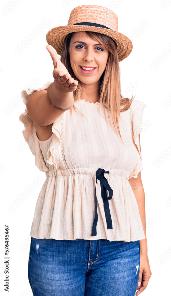 Young beautiful woman wearing summer hat and t-shirt smiling friendly offering handshake as greeting and welcoming. successful business.