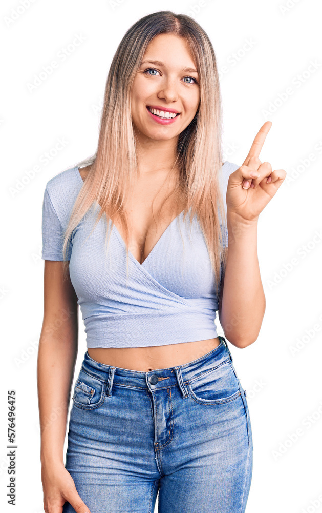 Young beautiful blonde woman wearing casual clothes showing and pointing up with finger number one while smiling confident and happy. Young beautiful blonde woman wearing casual clothes showing and pointing up with finger number one while smiling confident and happy.