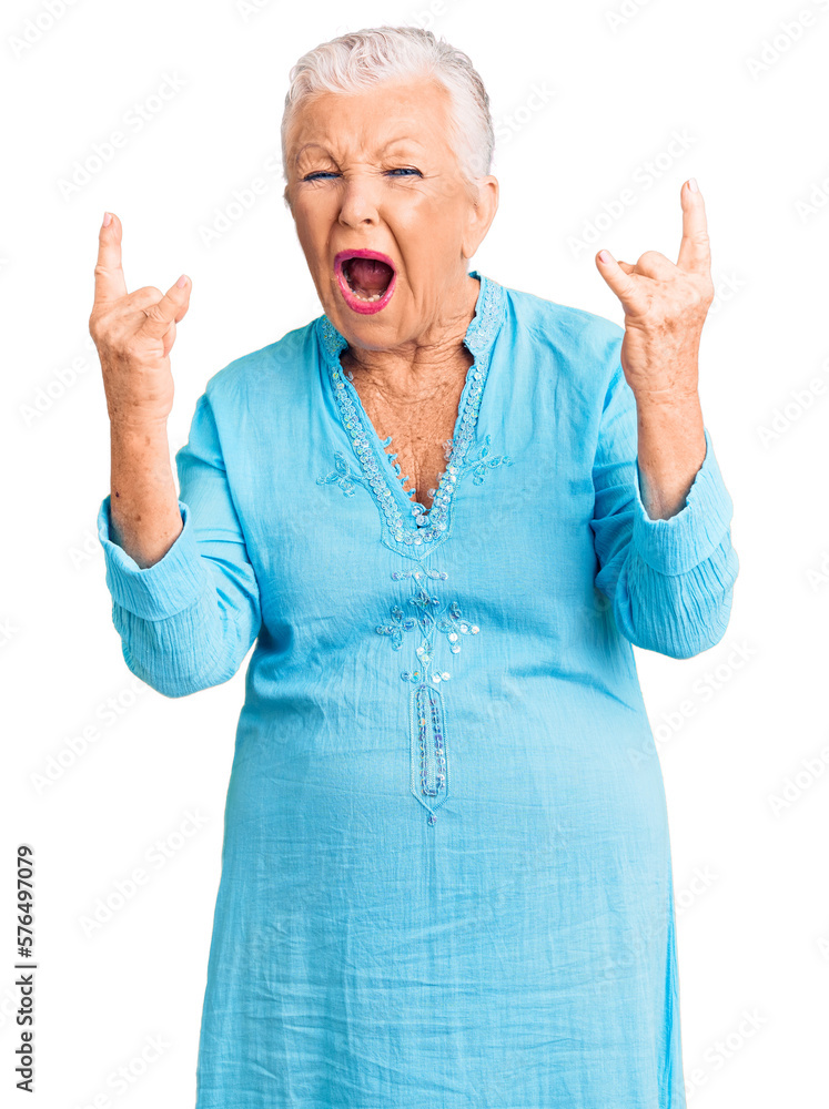 Senior beautiful woman with blue eyes and grey hair wearing summer dress shouting with crazy expression doing rock symbol with hands up. music star. heavy concept. Senior beautiful woman with blue eyes and grey hair wearing summer dress shouting with crazy expression doing rock symbol with hands up. music star. heavy concept.