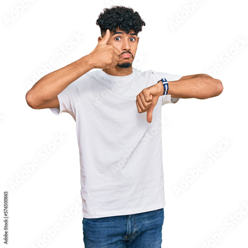 Young arab man wearing casual white t shirt doing thumbs up and down, disagreement and agreement expression. crazy conflict