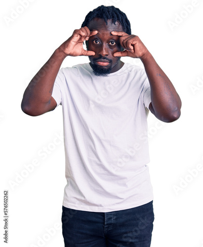 Young african american man with braids wearing casual white tshirt trying to open eyes with fingers, sleepy and tired for morning fatigue