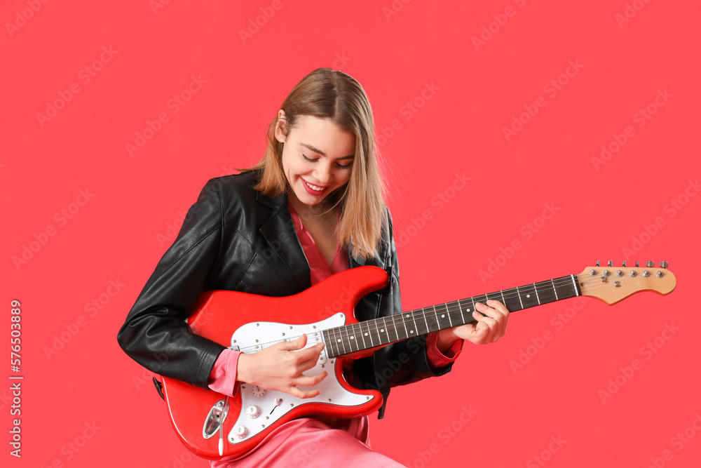 Fototapeta premium Young woman playing guitar on red background