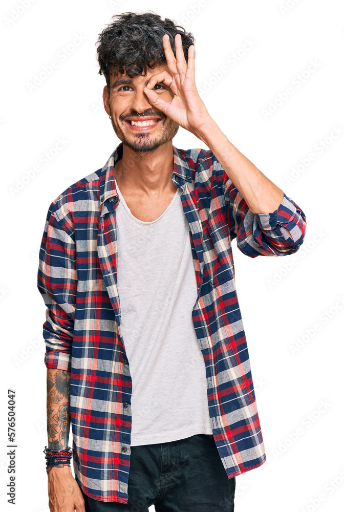 Young hispanic man wearing casual clothes doing ok gesture with hand smiling, eye looking through fingers with happy face. Young hispanic man wearing casual clothes doing ok gesture with hand smiling, eye looking through fingers with happy face.