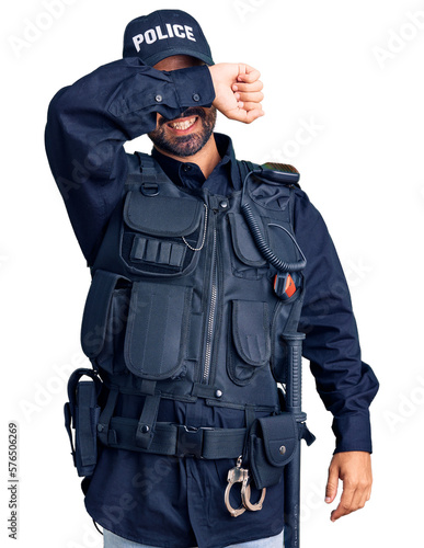 Young hispanic man wearing police uniform covering eyes with arm smiling cheerful and funny. blind concept.