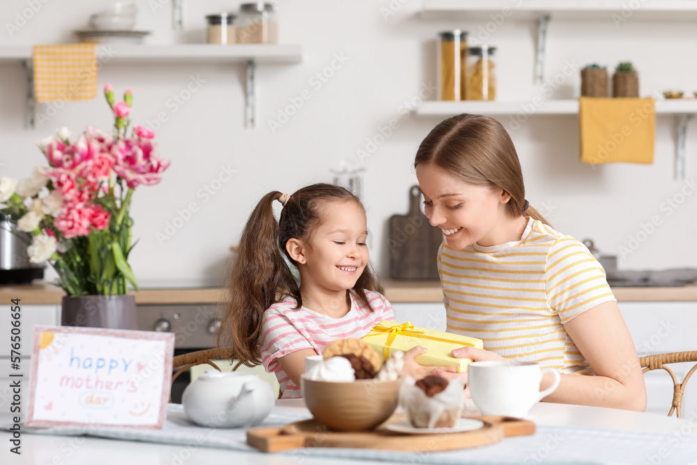 Cute little girl greeting her mother with gift in kitchen Cute little girl greeting her mother with gift in kitchen