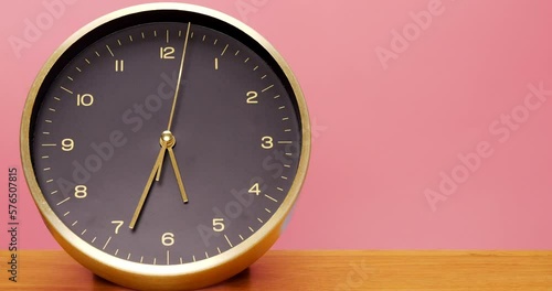 4K footage Time-lapse, black desk clock inlaid with gold frame is placed on the wooden floor with a pink background, walk and tell at 5 o'clock It takes 1 hour. photo