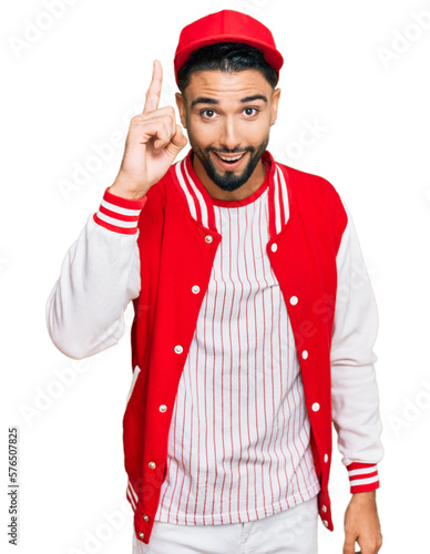 Young man with beard wearing baseball uniform pointing finger up with successful idea. exited and happy. number one.