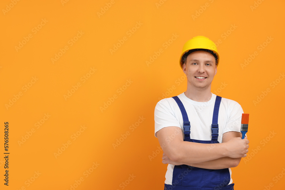 Happy worker holding paint brush near orange wall. Space for text