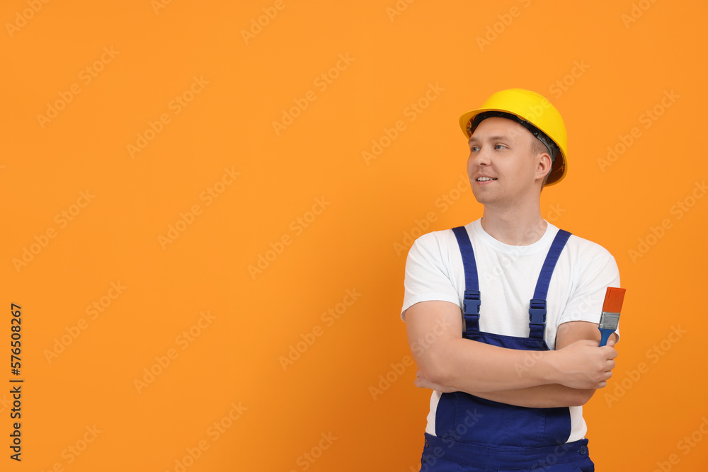 Worker holding paint brush near orange wall. Space for text