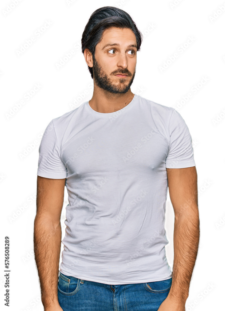Obraz premium Young hispanic man wearing casual white t shirt smiling looking to the side and staring away thinking.