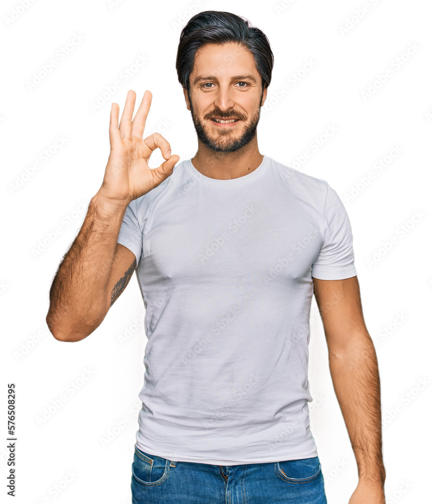 Young hispanic man wearing casual white t shirt smiling positive doing ok sign with hand and fingers. successful expression. Young hispanic man wearing casual white t shirt smiling positive doing ok sign with hand and fingers. successful expression.