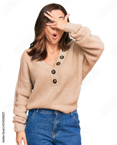 Young brunette woman wearing casual winter sweater peeking in shock covering face and eyes with hand, looking through fingers with embarrassed expression.
