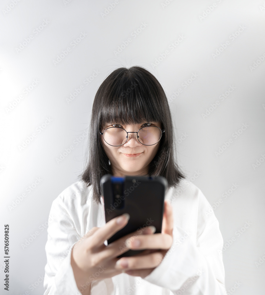 Isolated Pretty Asian glasses woman looks at camera and holds mobile phone in her hand on white background in studio light.