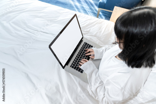 Topview of Glasses Asian cute woman works with laptop white screen on the bed in Work From Home period. © Surachetsh