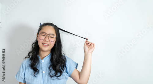 A young asian girl touch her hair smoothly with a big smile on her face. She is wearing a light blue shirt and glasses.