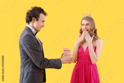 Young man greeting his prom date with gift on yellow background