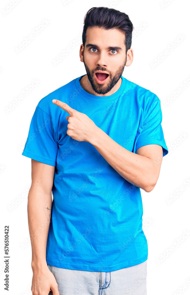 Young handsome man with beard wearing casual t-shirt surprised pointing with finger to the side, open mouth amazed expression. Young handsome man with beard wearing casual t-shirt surprised pointing with finger to the side, open mouth amazed expression.