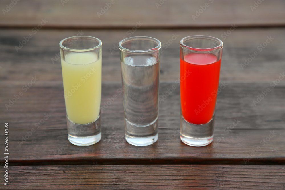 Shots with lime juice, tequila and sangria as colors of mexican flag on wooden table. Traditional serving Shots with lime juice, tequila and sangria as colors of mexican flag on wooden table. Traditional serving