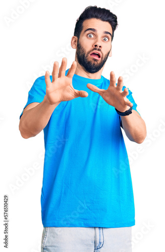 Young handsome man with beard wearing casual t-shirt afraid and terrified with fear expression stop gesture with hands, shouting in shock. panic concept.