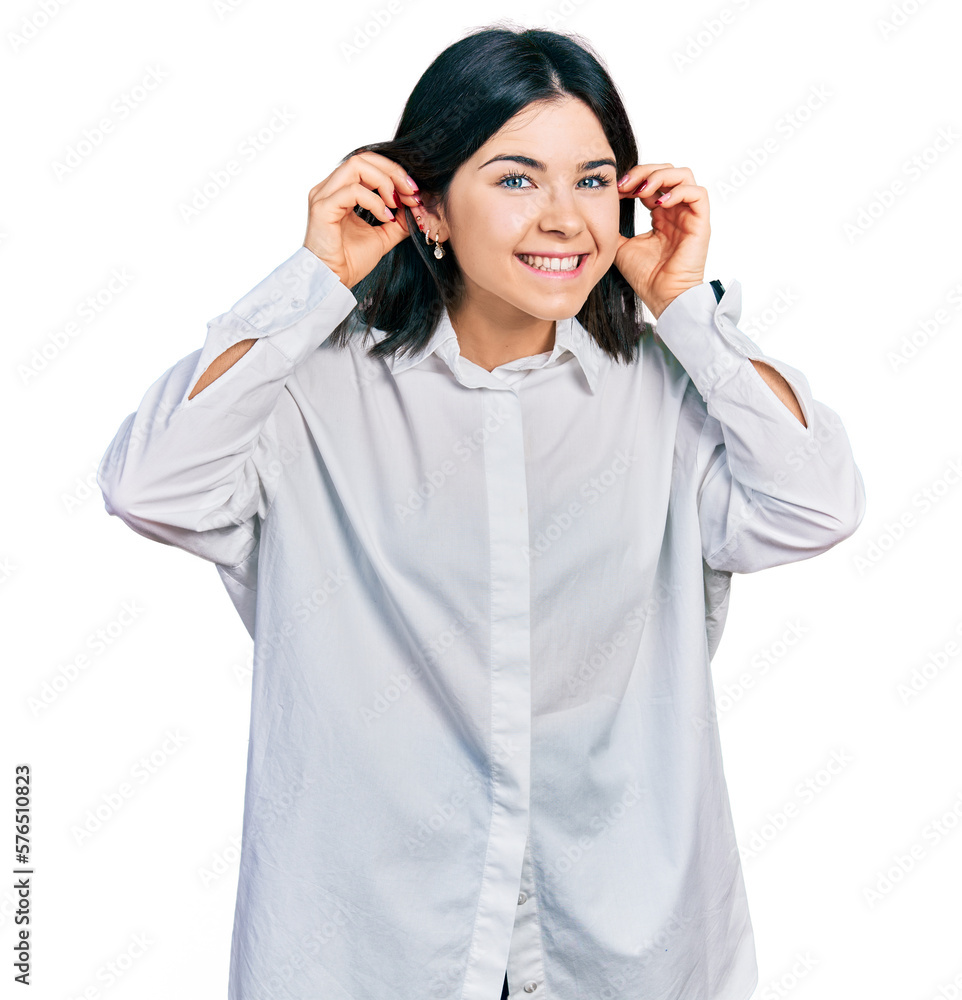 Young brunette woman with blue eyes wearing oversize white shirt smiling pulling ears with fingers, funny gesture. audition problem Young brunette woman with blue eyes wearing oversize white shirt smiling pulling ears with fingers, funny gesture. audition problem