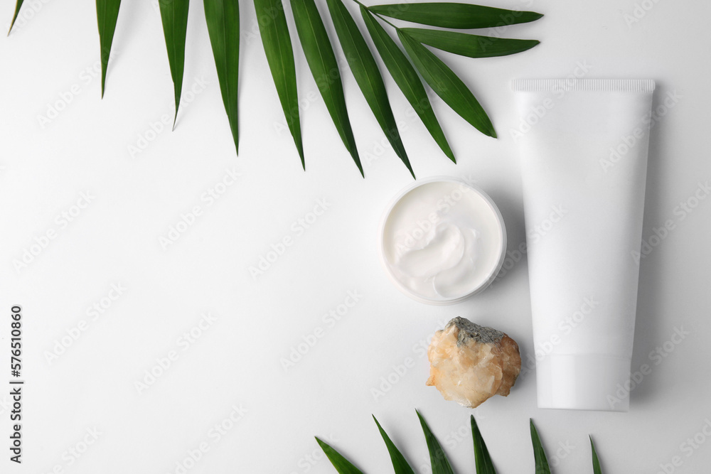 Cosmetic products, quartz gemstone and palm leaves on white background, flat lay. Space for text