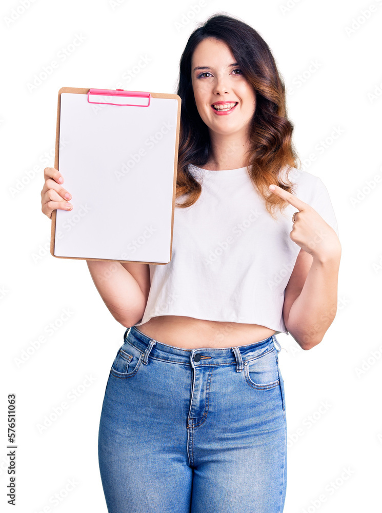 Beautiful young brunette woman holding clipboard with blank space smiling happy pointing with hand and finger Beautiful young brunette woman holding clipboard with blank space smiling happy pointing with hand and finger