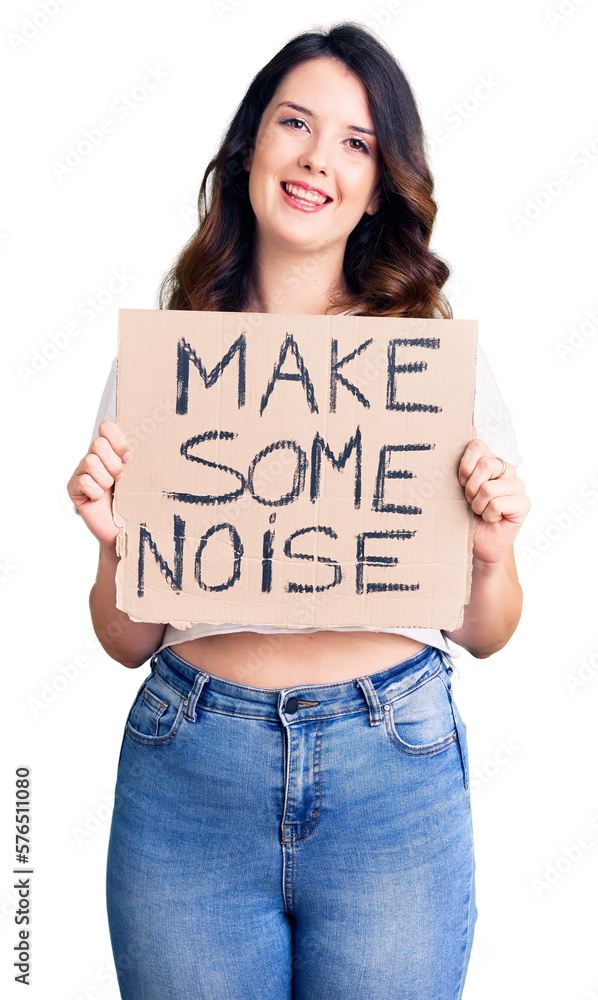Beautiful young brunette woman holding make some noise banner looking positive and happy standing and smiling with a confident smile showing teeth Beautiful young brunette woman holding make some noise banner looking positive and happy standing and smiling with a confident smile showing teeth