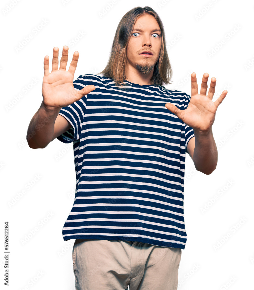 Fototapeta premium Handsome caucasian man with long hair wearing casual striped t-shirt afraid and terrified with fear expression stop gesture with hands, shouting in shock. panic concept.