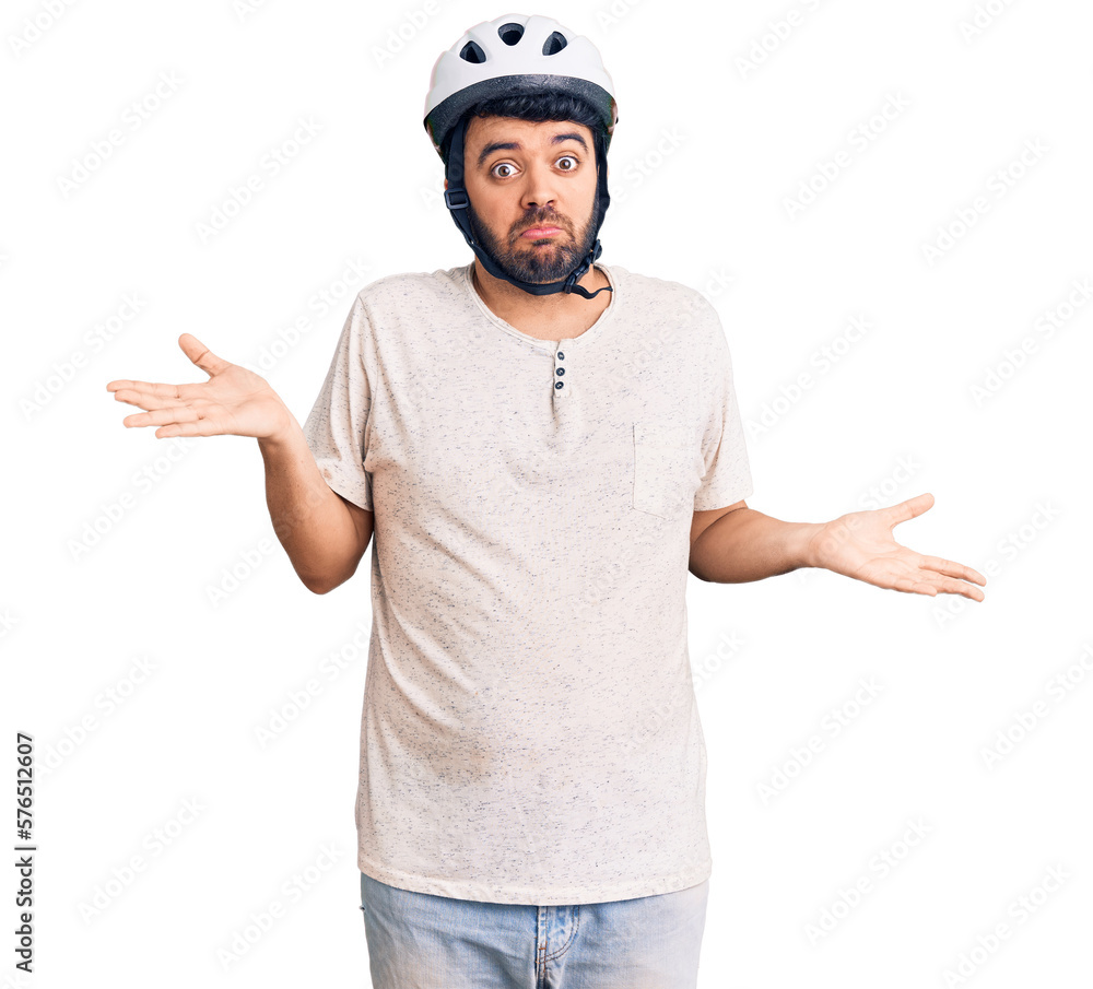 Young hispanic man wearing bike helmet clueless and confused expression with arms and hands raised. doubt concept. Young hispanic man wearing bike helmet clueless and confused expression with arms and hands raised. doubt concept.