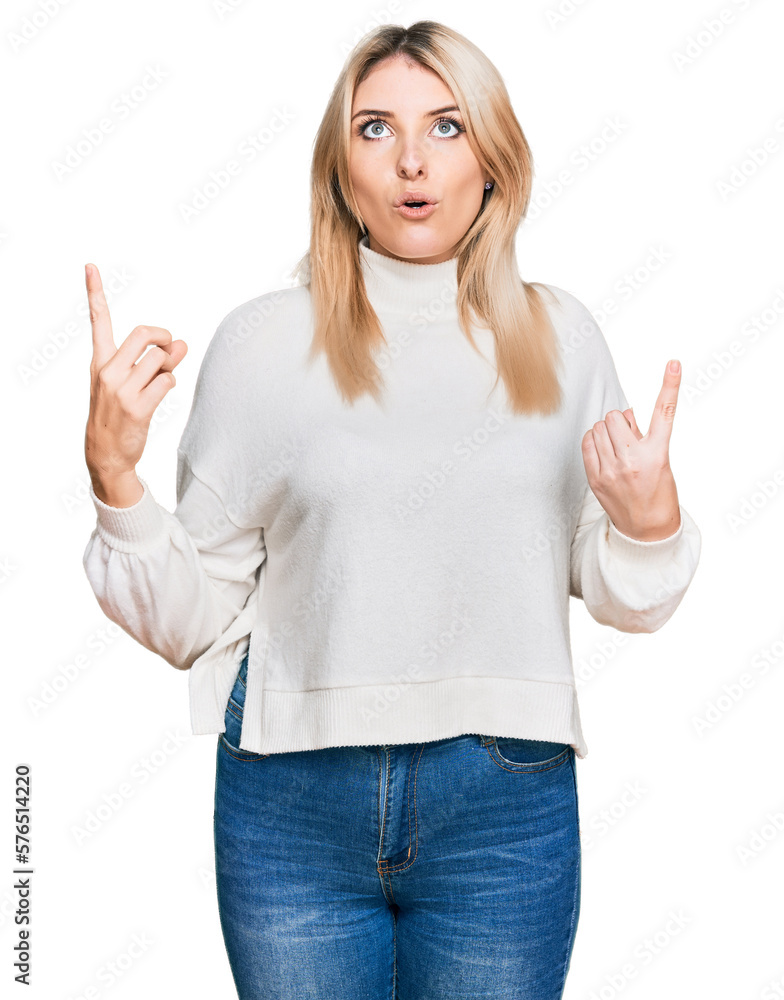 Young caucasian woman wearing casual winter sweater amazed and surprised looking up and pointing with fingers and raised arms.