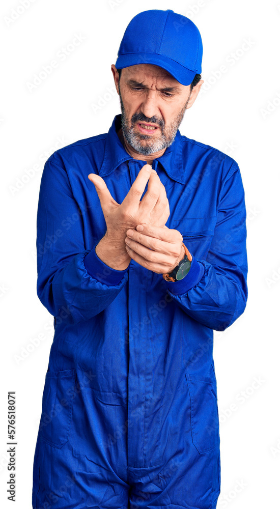Middle age handsome man wearing mechanic uniform suffering pain on hands and fingers, arthritis inflammation Middle age handsome man wearing mechanic uniform suffering pain on hands and fingers, arthritis inflammation