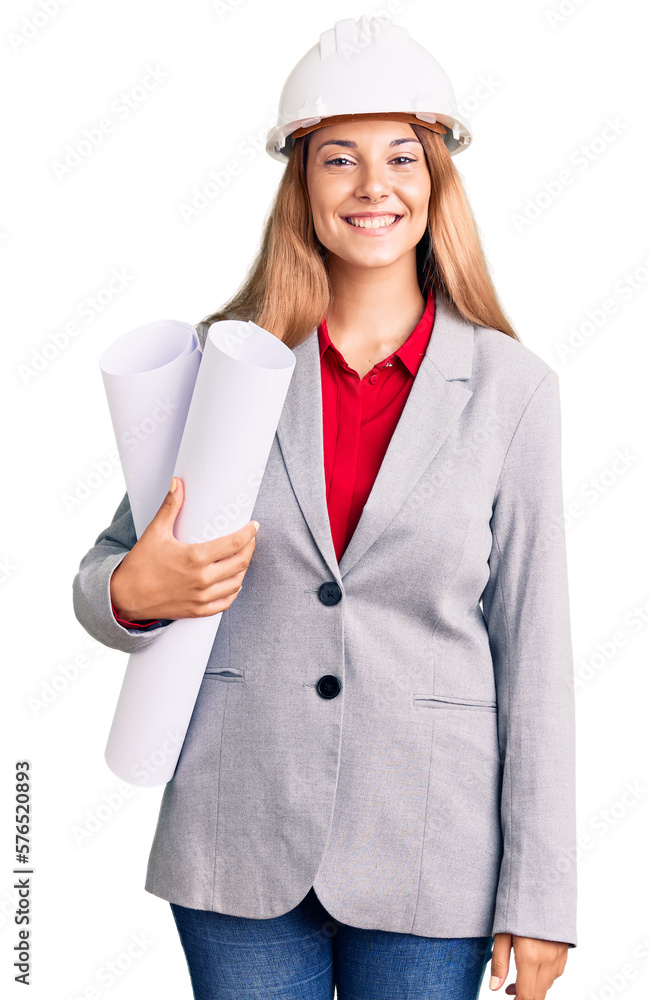 Beautiful young woman wearing architect hardhat holding build project looking positive and happy standing and smiling with a confident smile showing teeth Beautiful young woman wearing architect hardhat holding build project looking positive and happy standing and smiling with a confident smile showing teeth