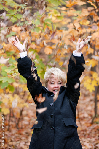 Happy blond woman throwing colorful Autumn leaves in the air.