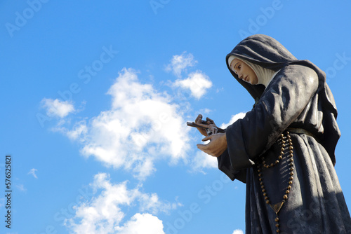 Estátua de Santa Rita de Cássia e céu azul com nuvens ao fundo photo
