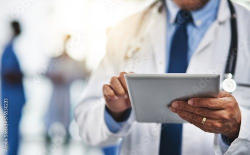 Keeping his patients file close to him with wireless technology. Cropped shot of a doctor using a digital tablet with his colleagues in the background.