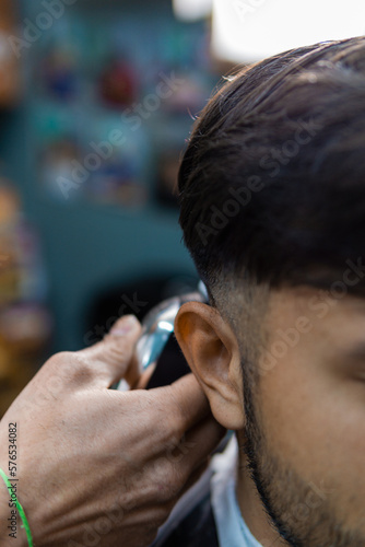 Latin man haircut with shaving machine, focus on the ear