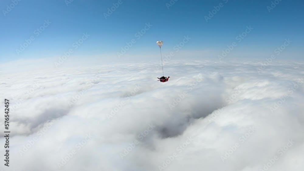 Tandem skydive high above white puffy clouds in blue sky; adrenaline sport Tandem skydive high above white puffy clouds in blue sky; adrenaline sport