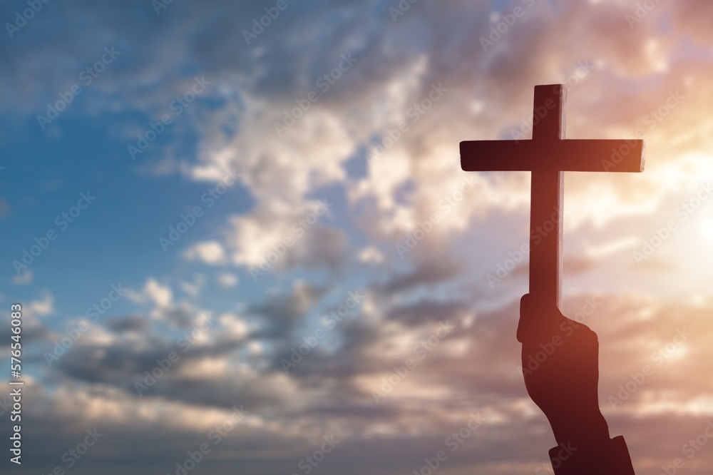 A hand holds a wooden cross on sky background