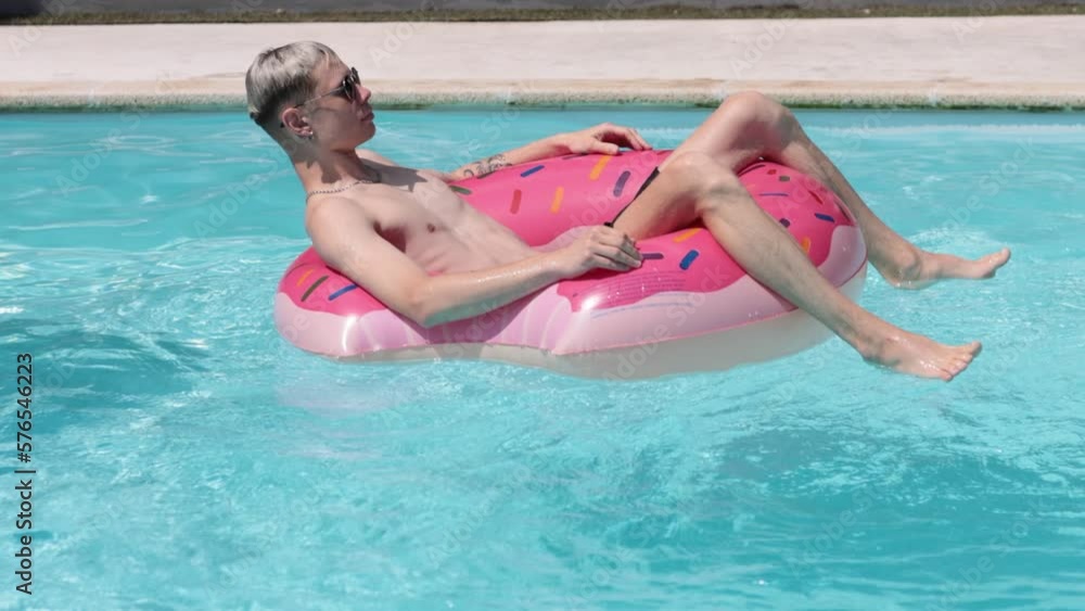 Young handsome man in shorts and sunglasses relaxing on floating water ring. slow motion Young handsome man in shorts and sunglasses relaxing on floating water ring. slow motion