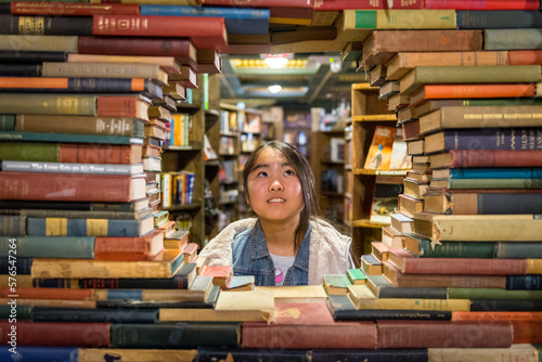 Young asian girl standing behind window created by stack of books